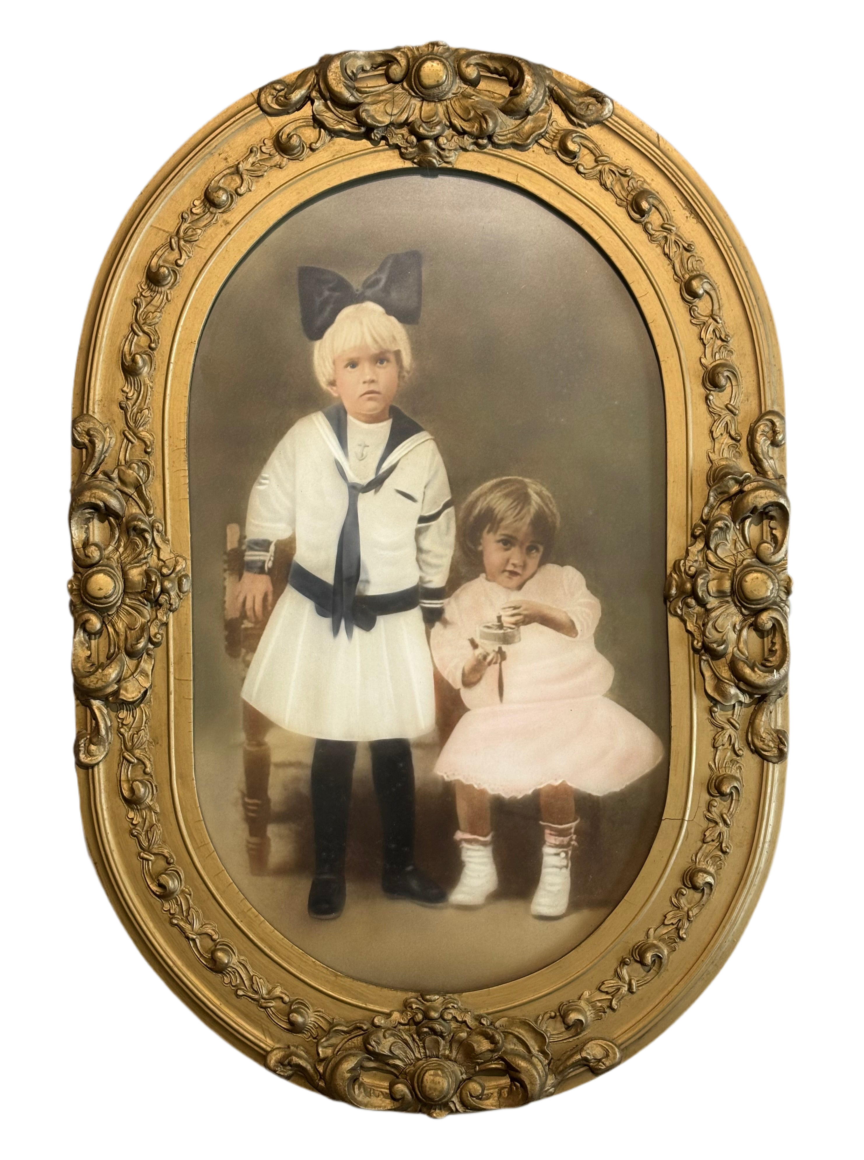 Vintage photograph of two children in formal attire inside an ornate gold frame.