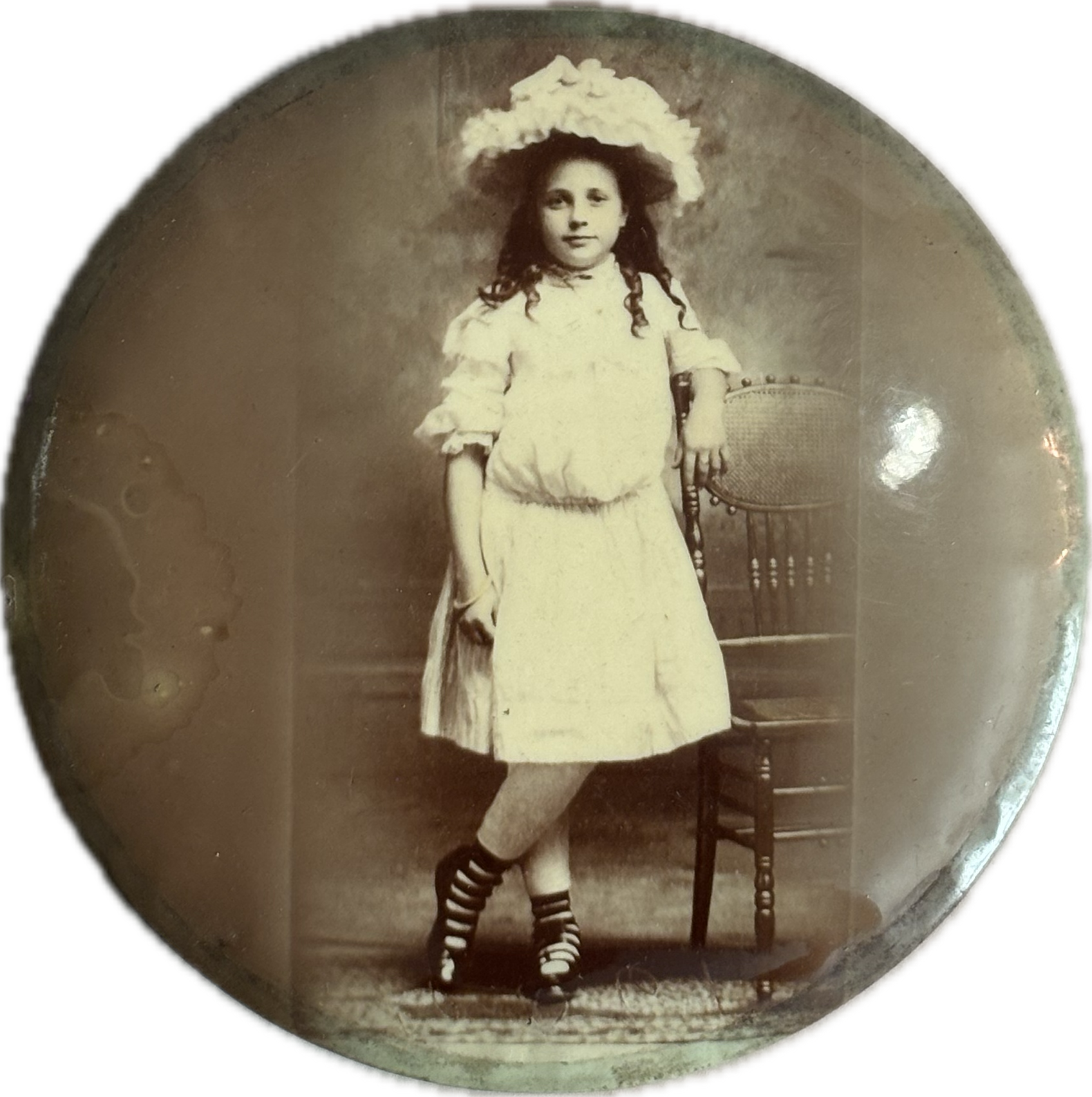 Vintage photograph of a young girl in a white dress and hat, standing on a chair.